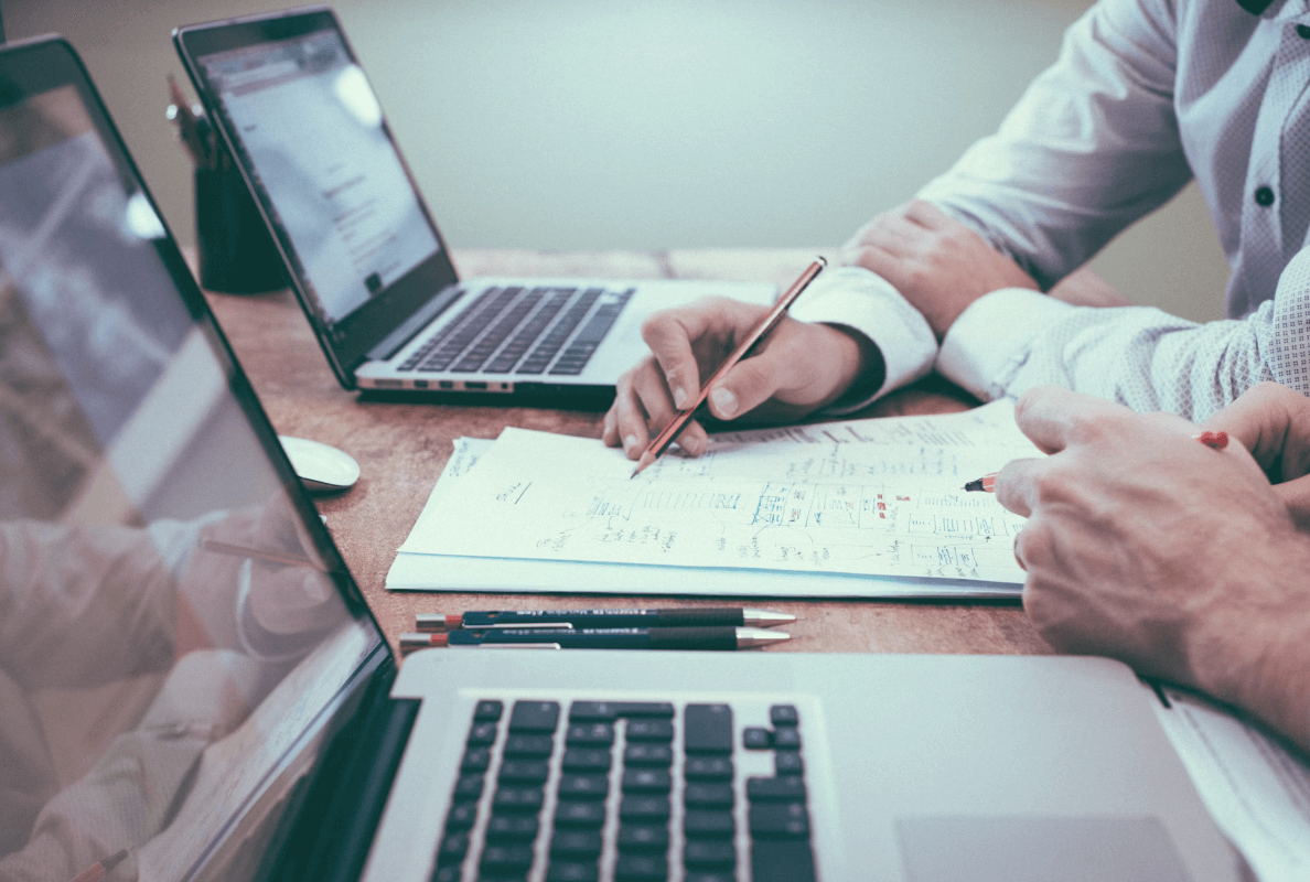 Advisory Services for Businesses. Close up of hands pointing at notes on paper with laptops in foreground and background