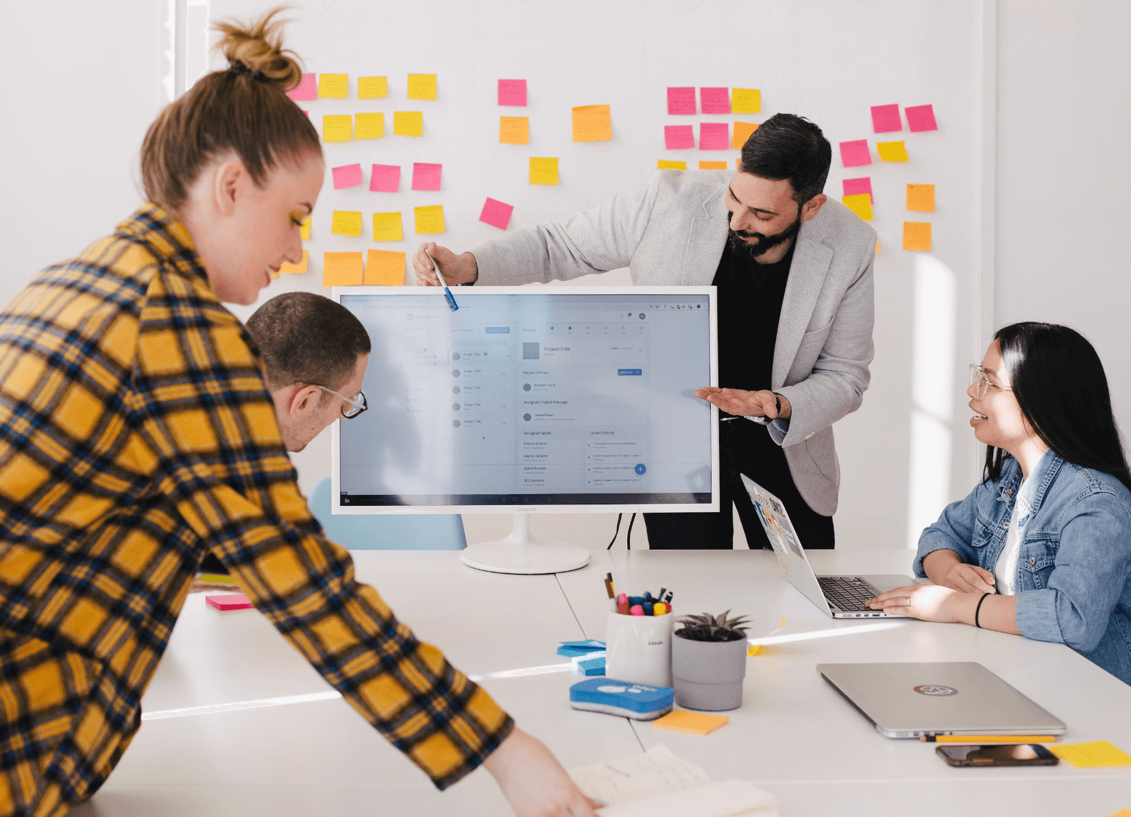 Person presenting from behind a computer screen with board full of sticky notes in background