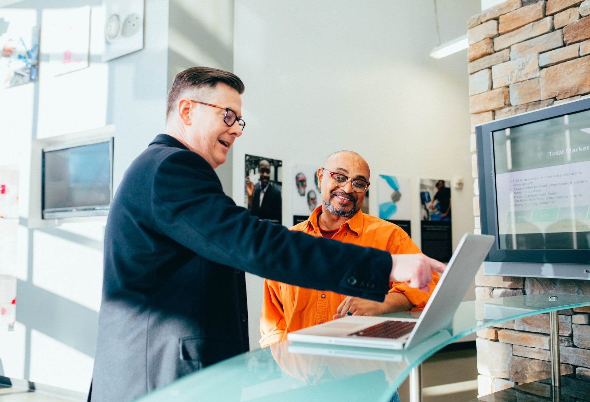 Bevan Buckland Accountants. Man in suit pointing to laptop with smiling man in orange shirt next to him